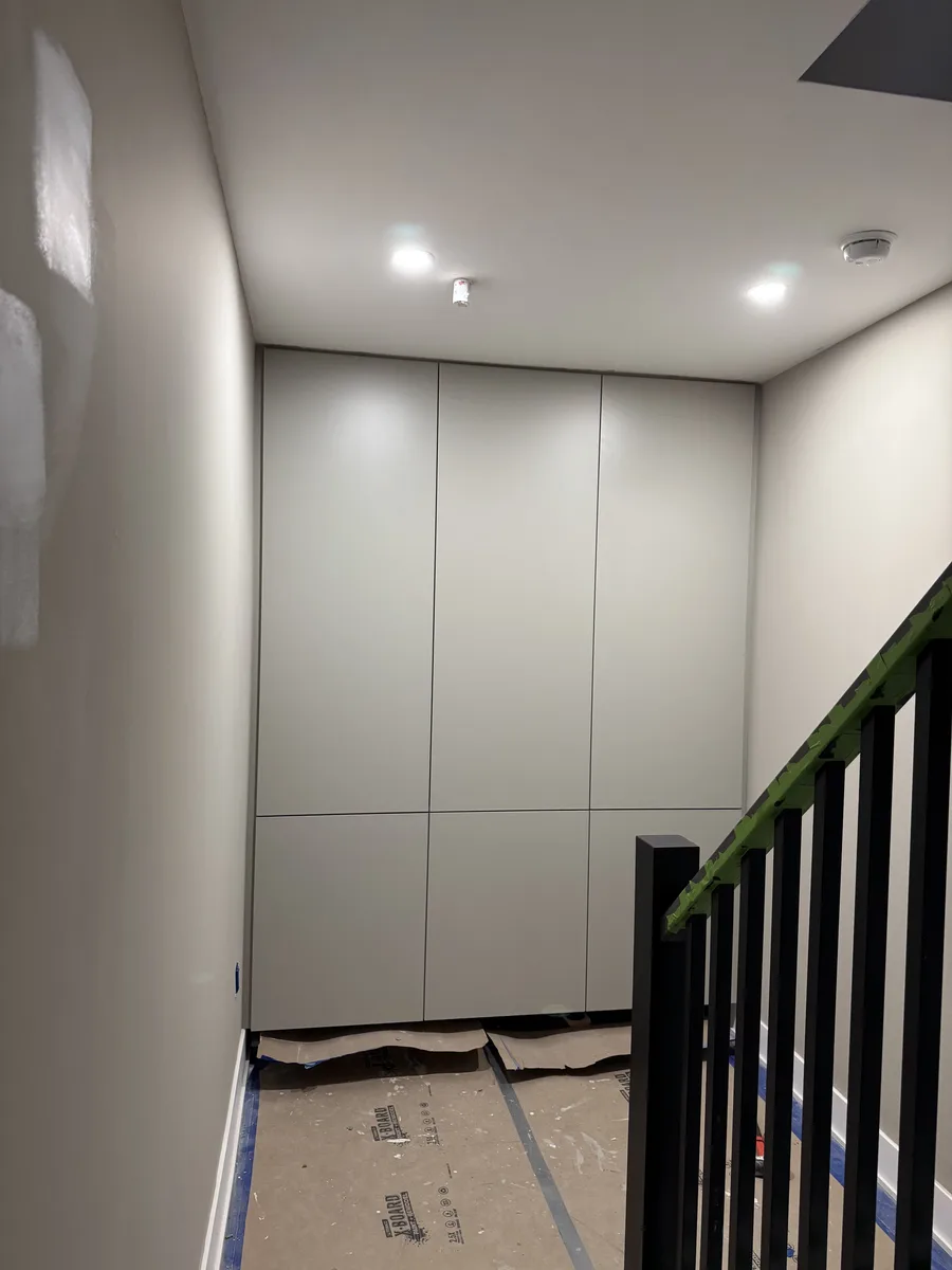 Finished storage wall seen from staircase — grey flush-panel cabinets, black metal railing with oak handrail, LVP flooring